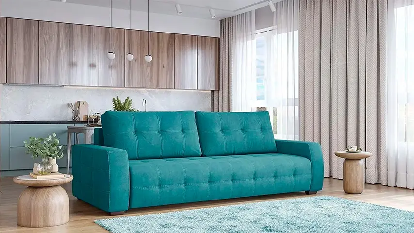 مبل سهنفره فیروزهای با طراحی مدرن و دوخت مربعی روی نشیمن، قرارگرفته در نشیمنِ روبهروی آشپزخانه اوپن با میزهای چوبی کوچک و پردههای بلند روشن.
